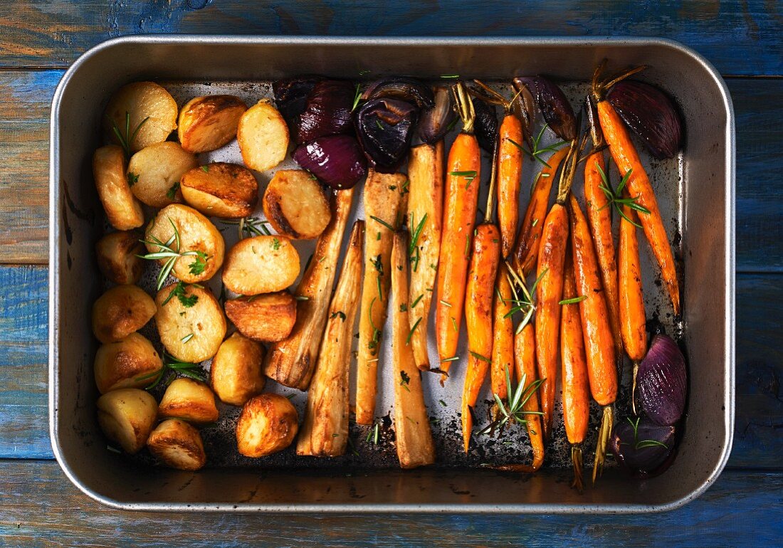 Roasted root vegetables and red onions in a roasting tin