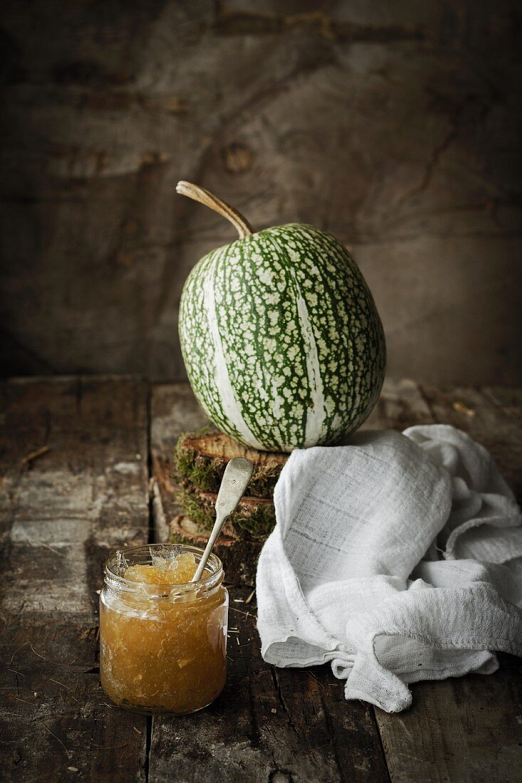 Ein Glas Kürbismarmelade vor frischem Kürbis