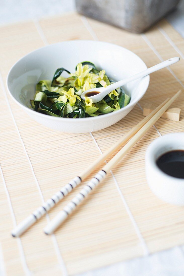 Zucchinispaghetti mit Blüten auf Bambusmatte mit Stäbchen (Asien)