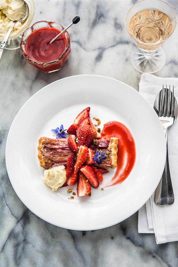 Ein Stück Rhabarbertarte mit frischen Erdbeeren, Borretschblüten, Mascarpone und Erdbeer-Rhabarber-Coulis