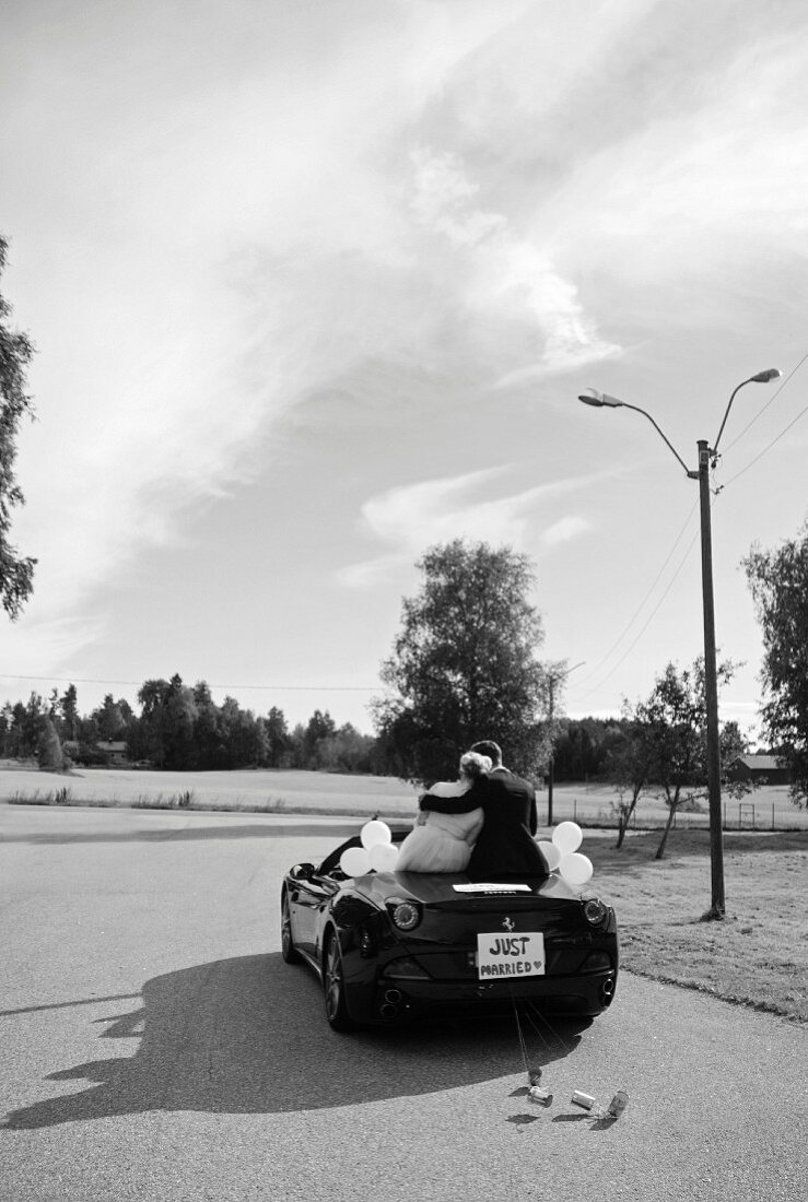 A bride and groom sitting in a convertible with a 'Just Married' sign (black-and-white shot)
