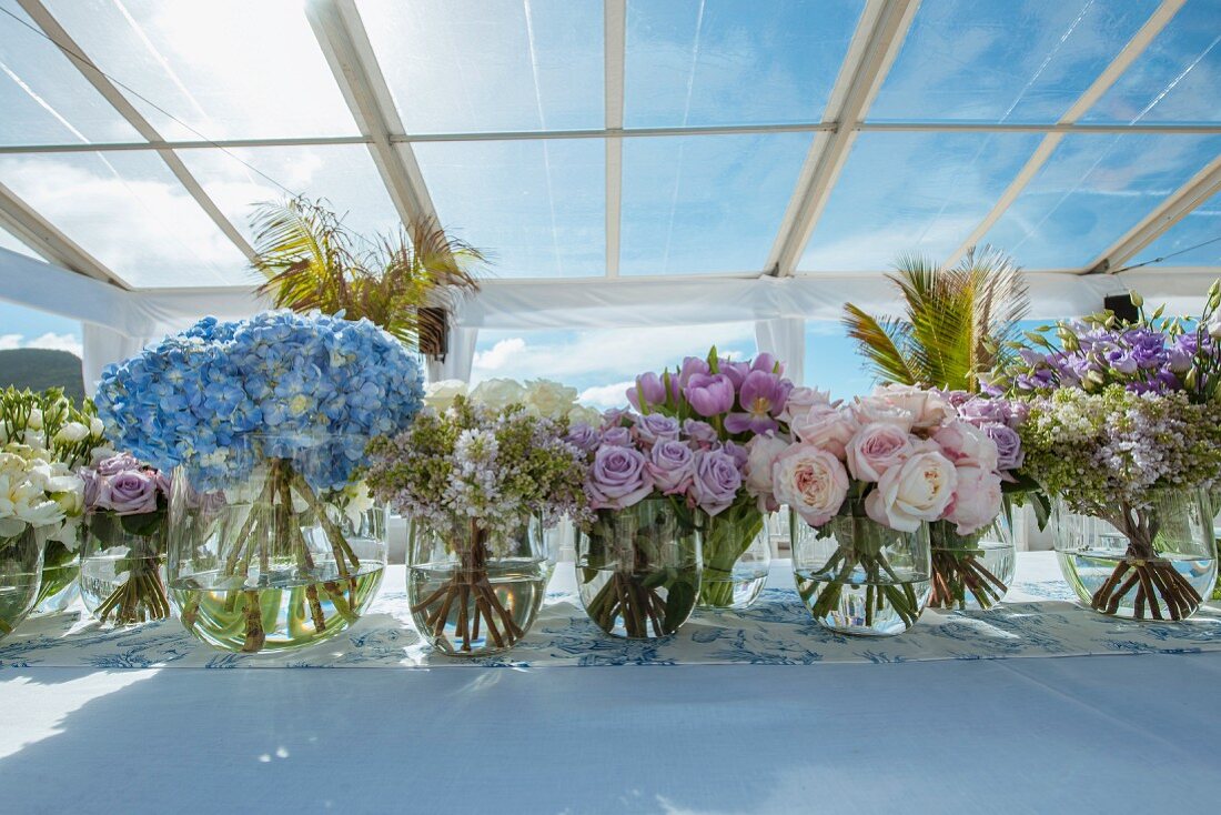 Verschiedene Blumensträusse in Glasvasen auf Tisch, Hochzeitsdekoration, in sonnigem Ambiente