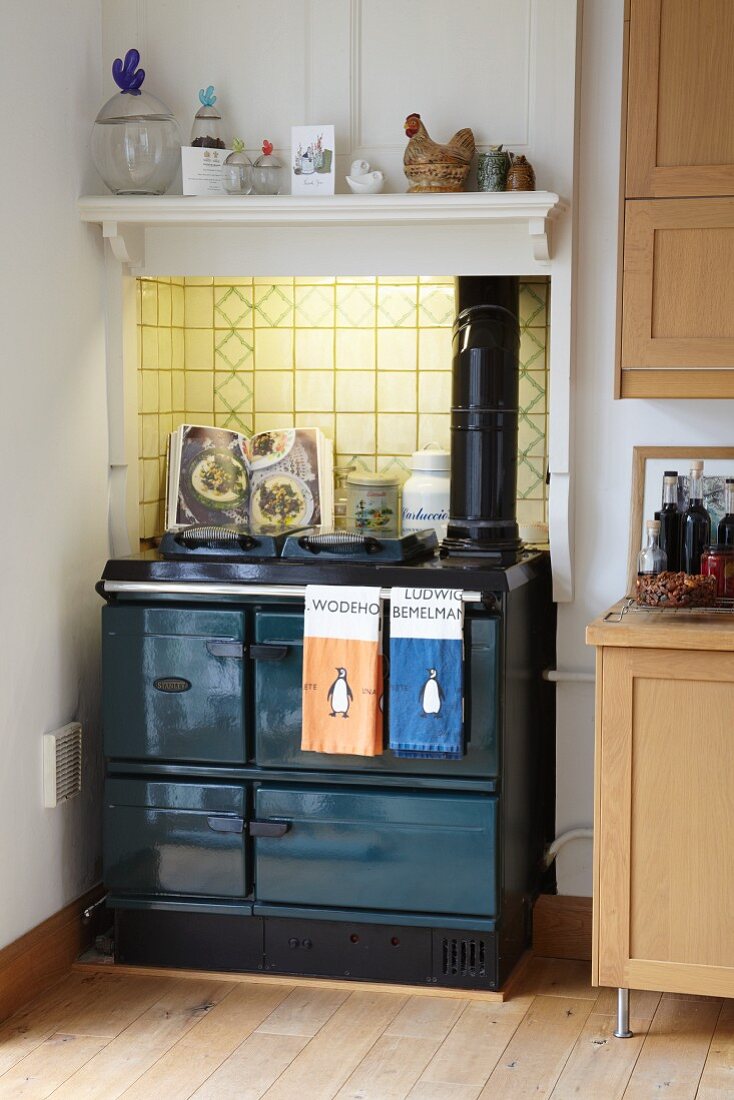 Kitchen cooker against vintage-style, illuminated wall tiles below glass jars on white bracket shelf