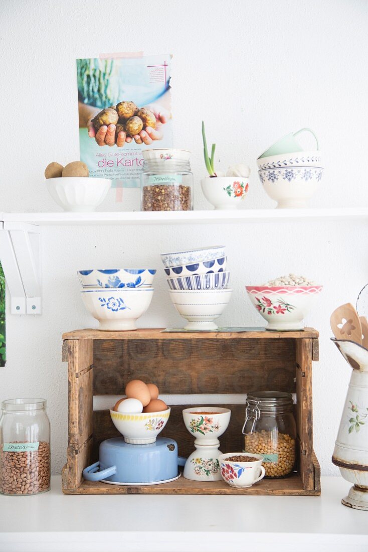 Rustic wine crate used as kitchen shelf and stacked white and blue bowls below white shelf in vintage-style ambiance