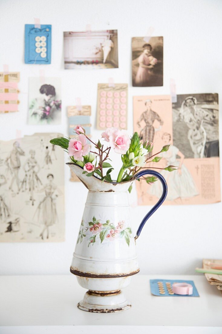Rose buds in vintage jug with floral motif in front of vintage postcards and magazine clippings