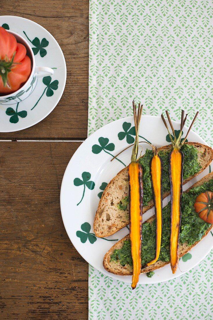 Slices of bread topped with pesto and roasted carrots on a plate with a clover leaf pattern