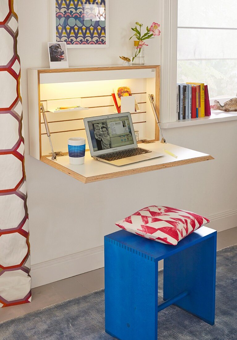 A simple, wall-mounted cupboard with a fold-down desk, indirect lighting and a laptop