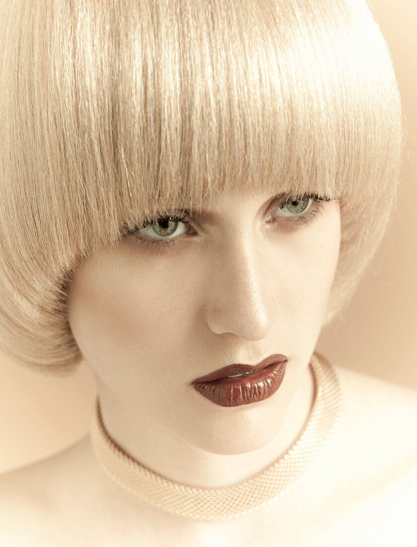 A young woman with platinum blonde pageboy hair style wearing a flat gold necklace