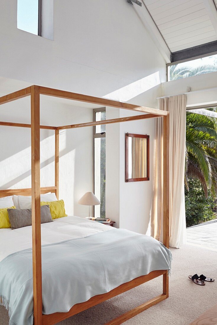 Wooden four-poster bed in bedroom with open French windows