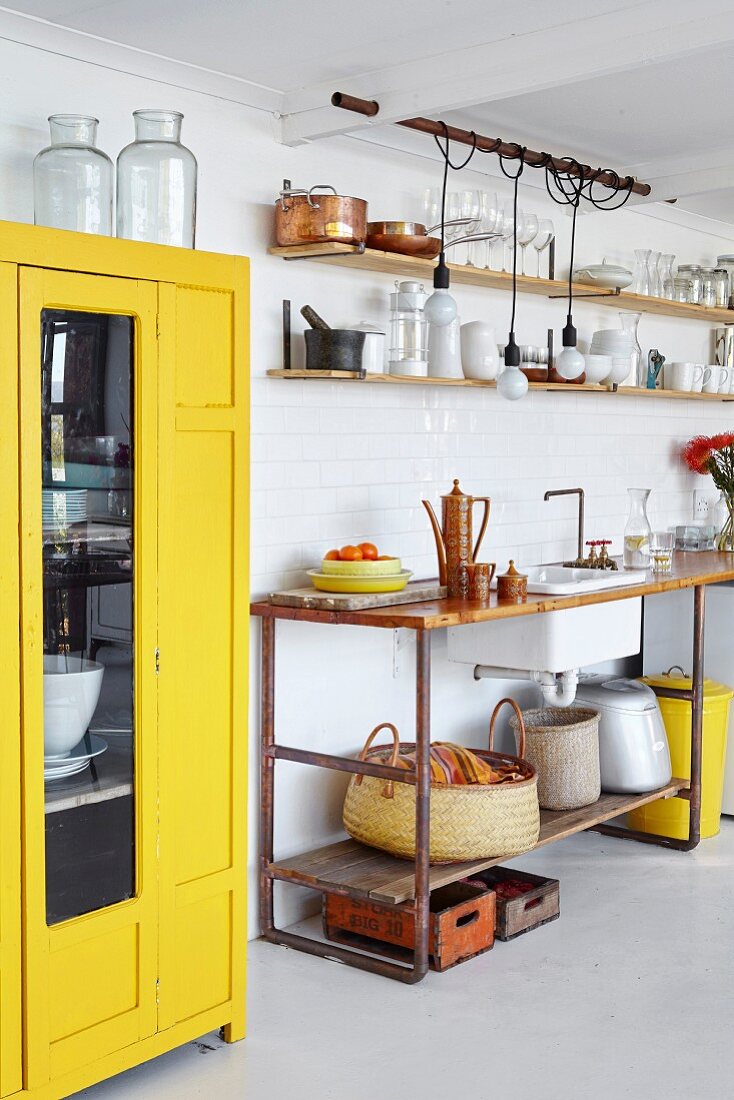Yellow cabinet with glass door next to kitchen counter with wooden worksurface on metal frame