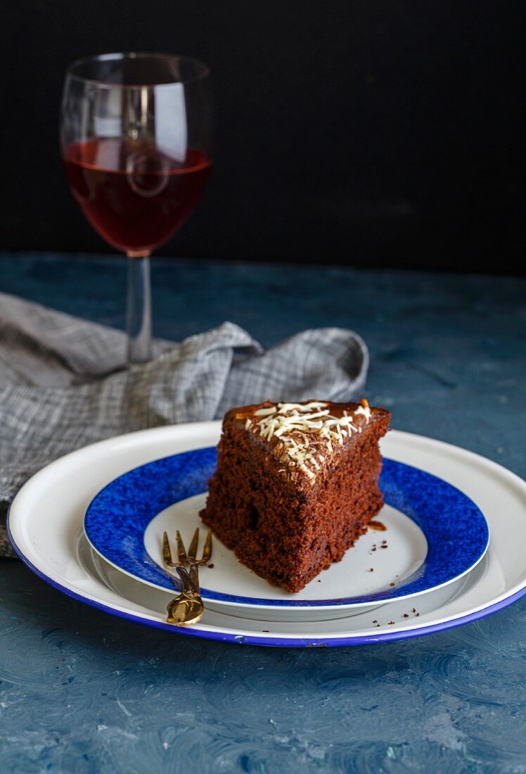 A slice of eggless chocolate cake on a plate with a glass of red wine