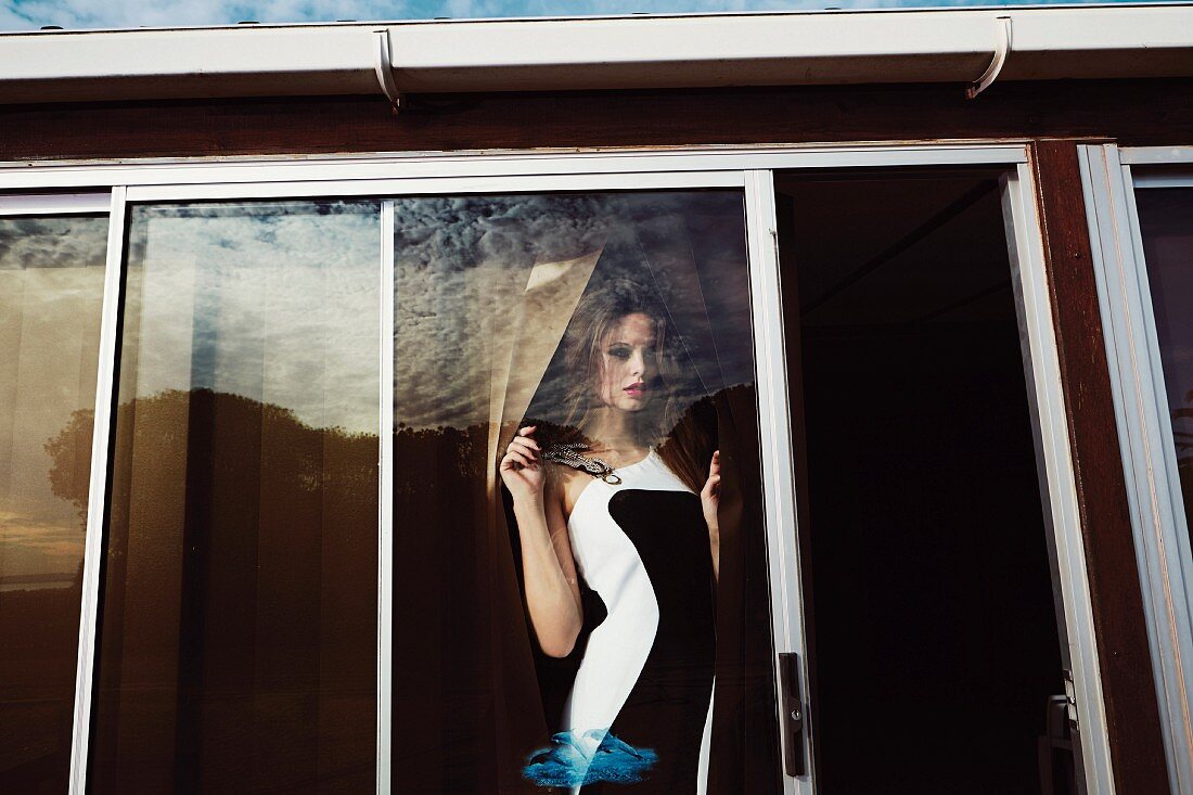 A young woman wearing a black and white dress behind terrace doors