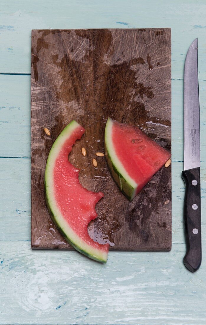 A half eaten slice of watermelon on a wooden board