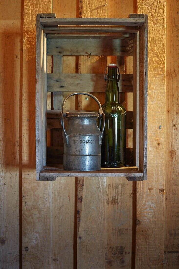 Alte Milchkanne und Flasche mit Bügelverschluss als Deko in Obstkiste an der Wand eines Holzhauses