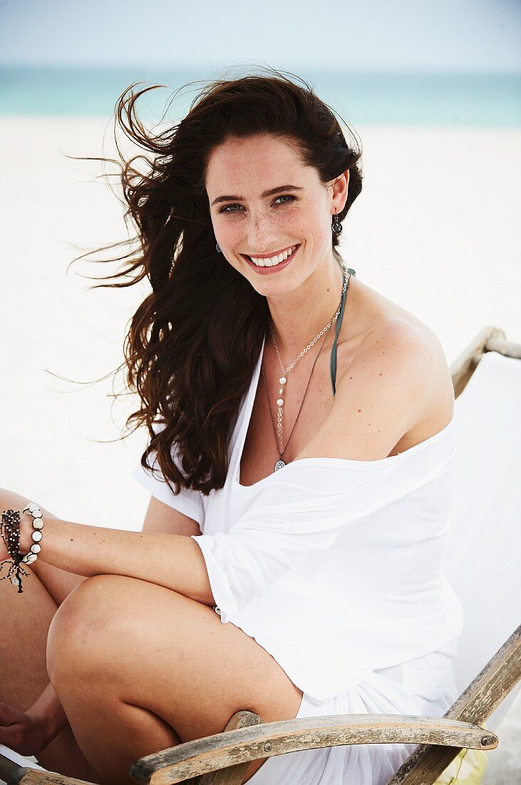 A brunette woman sitting in a deck chair will wearing a white oversized T-shirt