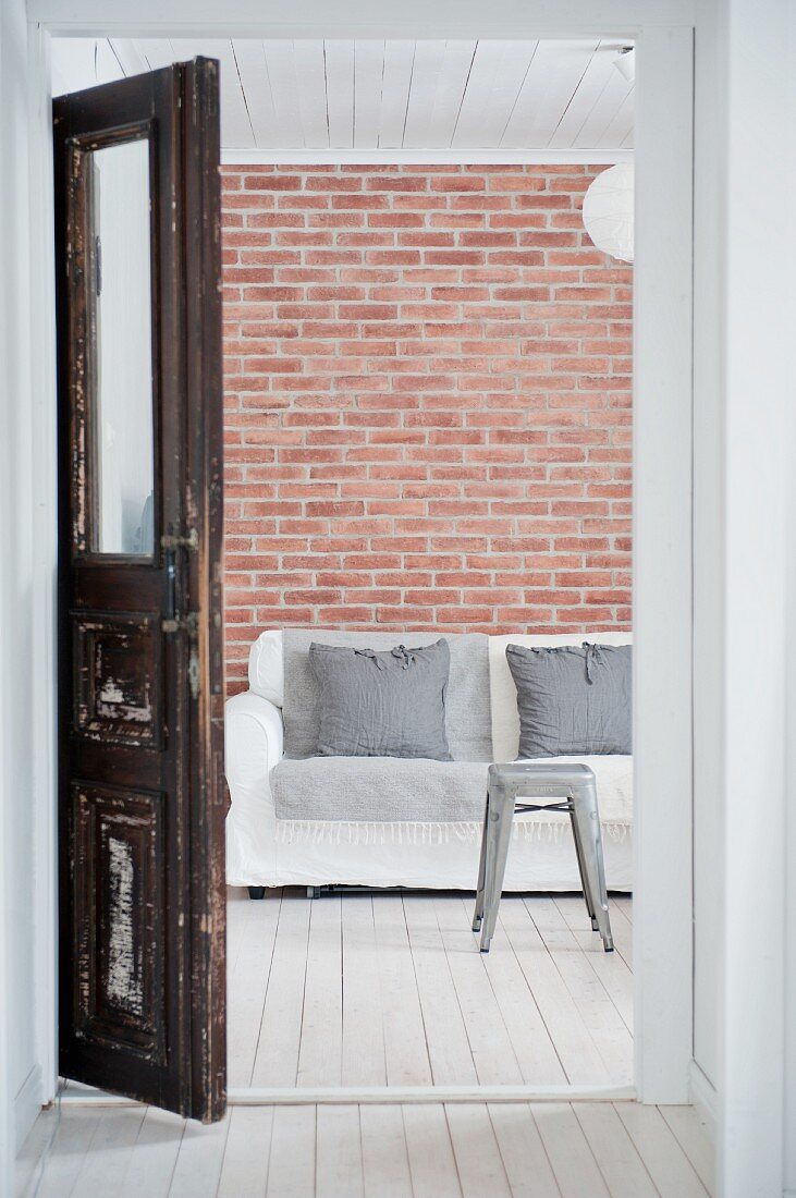 View of sofa against brick wall through old wooden door