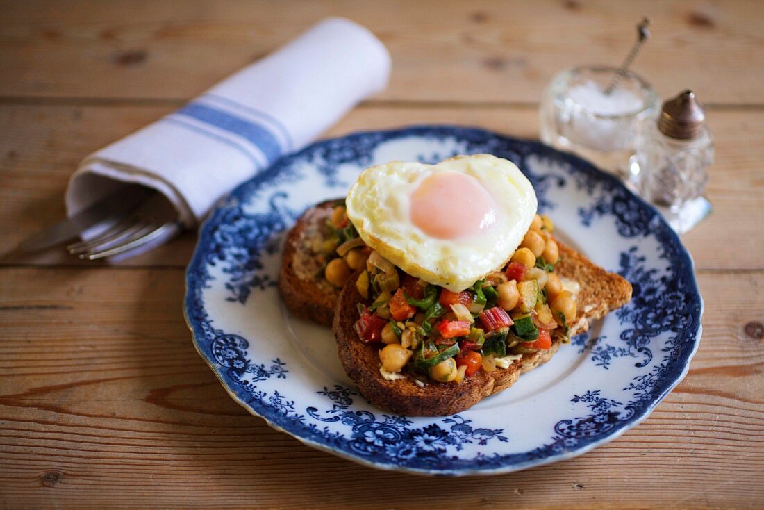 Toast mit Tomaten, Mangold, Kichererbsen und herzförmigem Spiegelei