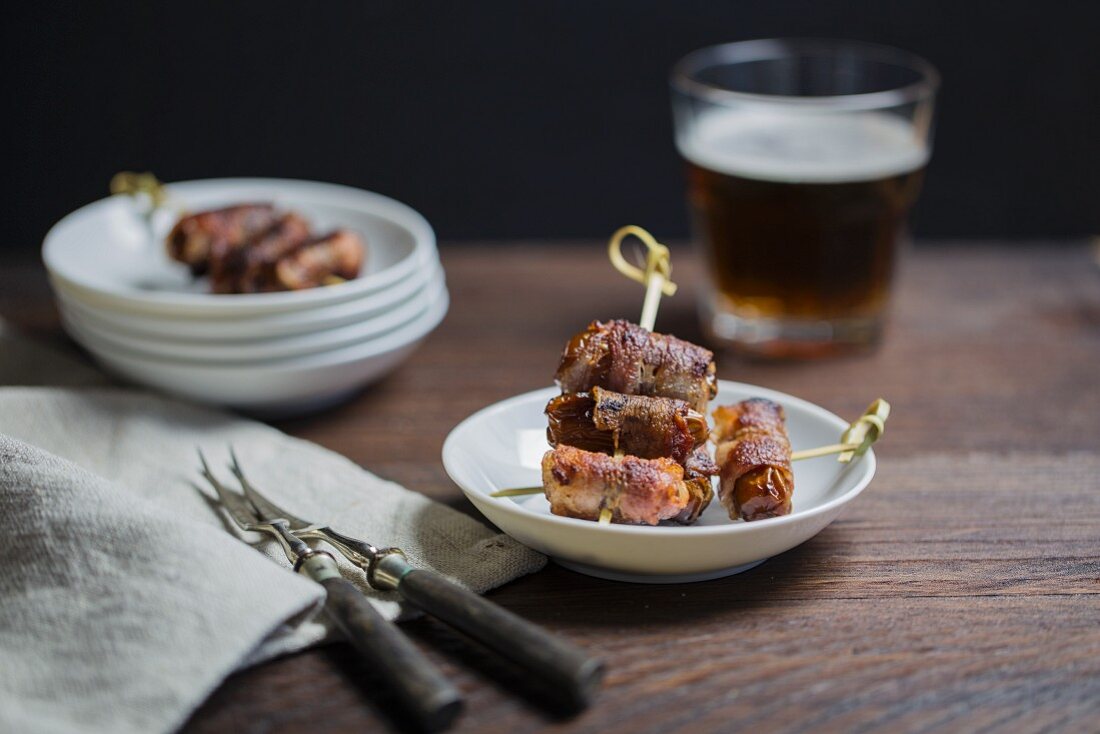 Dates wrapped in bacon served with a glass of beer