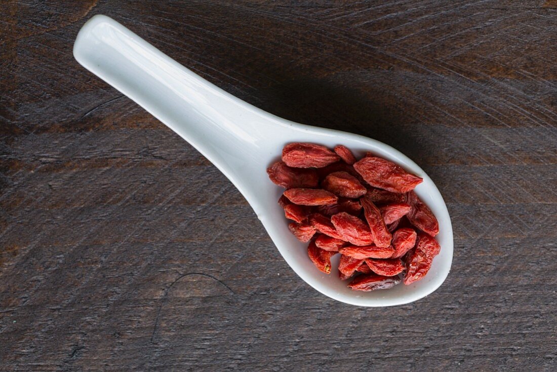 Goji berries on a porcelain spoon on a dark surface