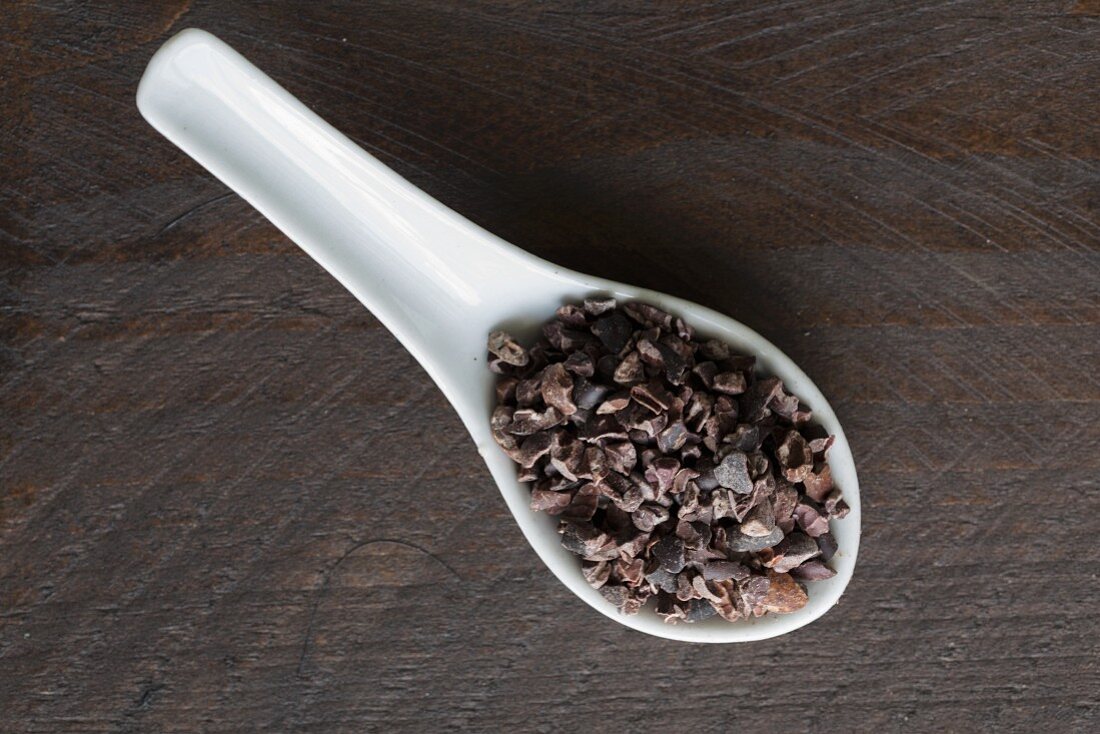 Cocoa nibs on a porcelain spoon on a dark surface