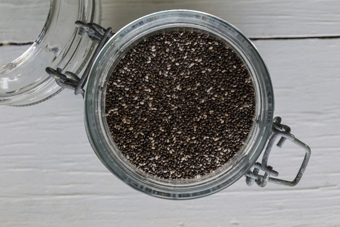 Chia seeds in a flip-top on a white wooden surface