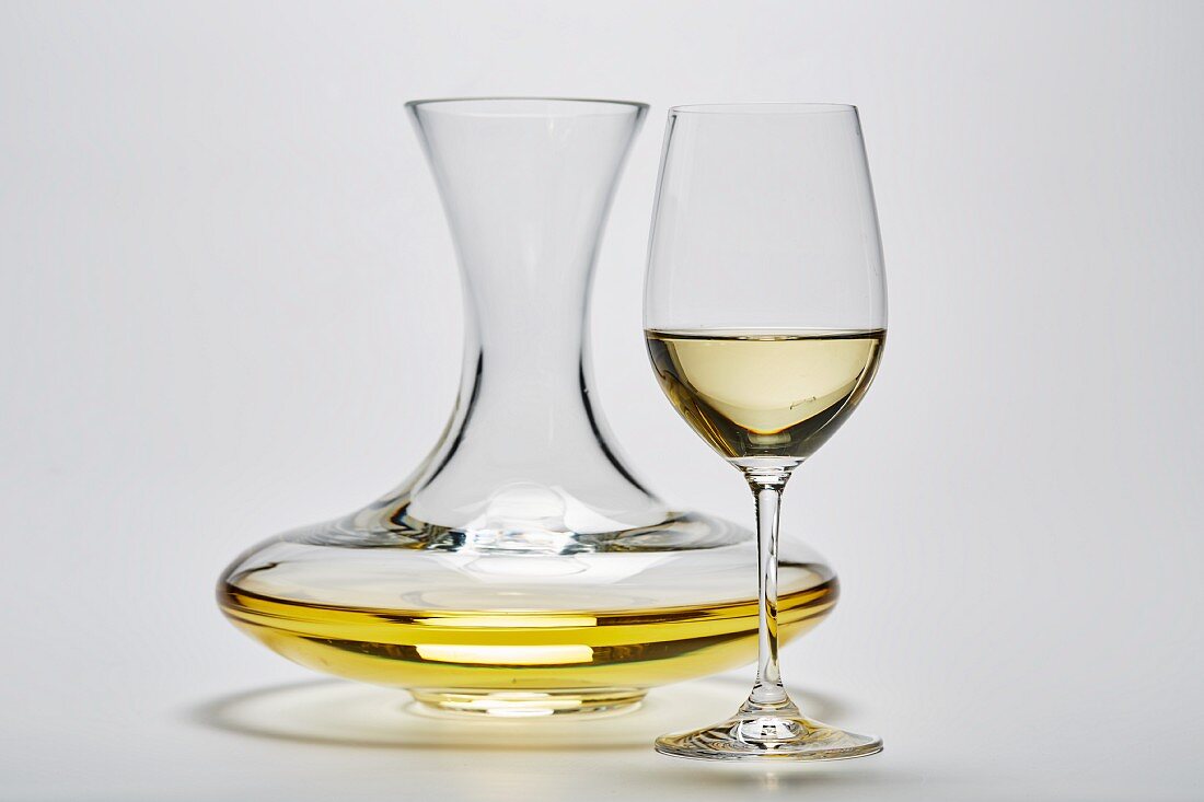 A glass carafe and a glass of white wine on a white surface