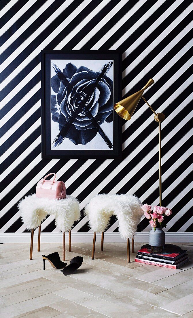 Two sheepskin-covered stools in front of black and white striped wallpaper in feminine interior