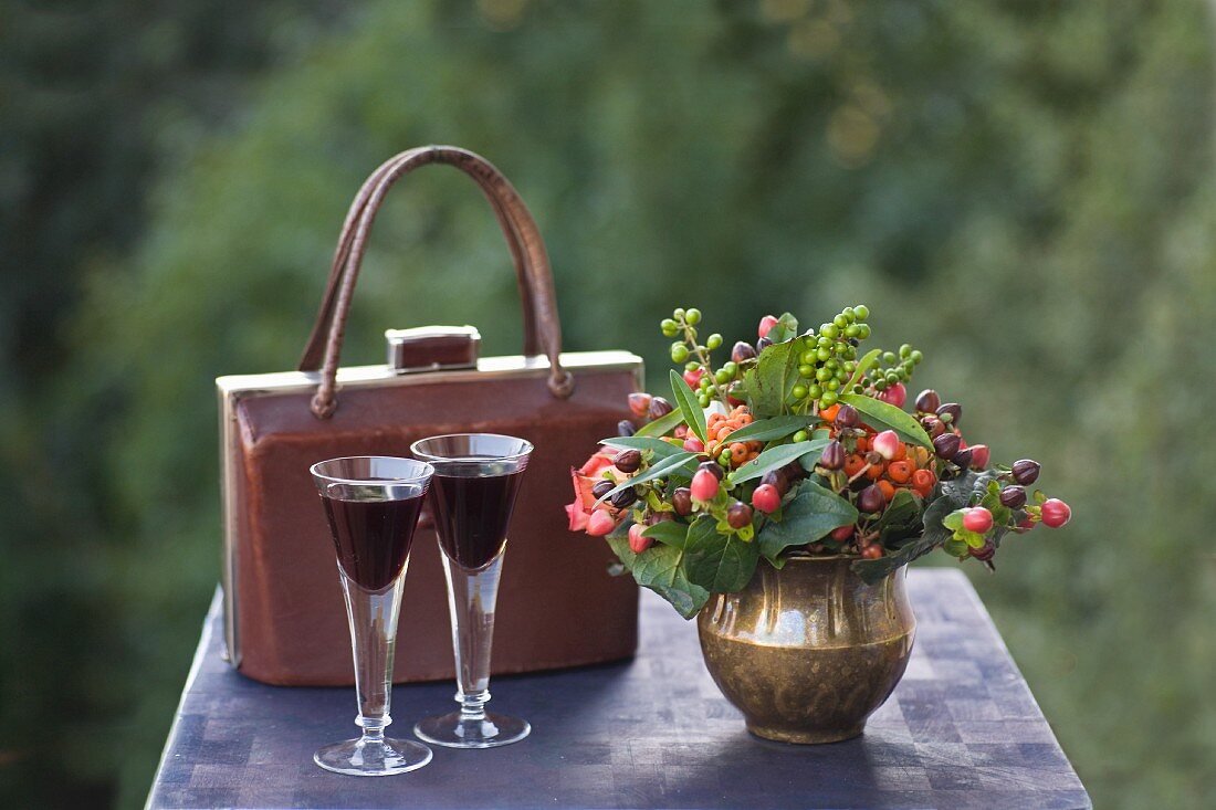 Autumn still-life arrangement with posy of berries in brass vase, vintage handbag and two aperitifs