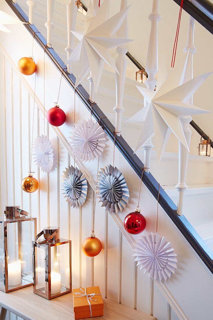A banister decorated with paper stars and Christmas tree baubles