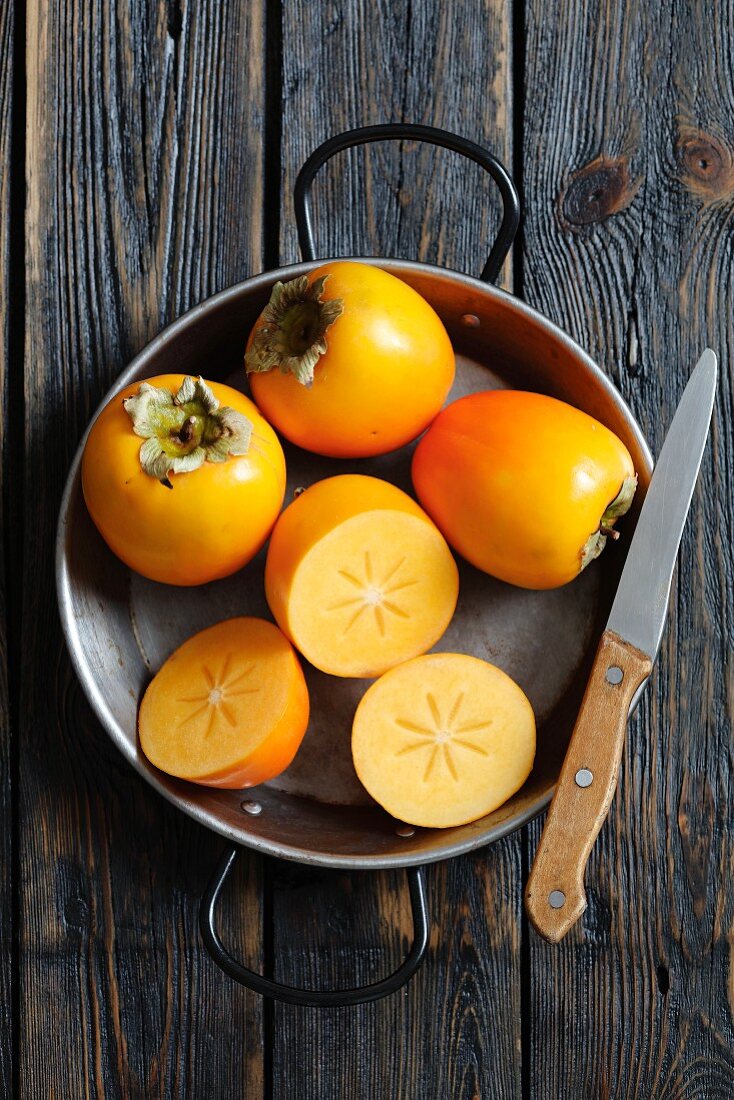 Persimmons, whole and halved, in a pan
