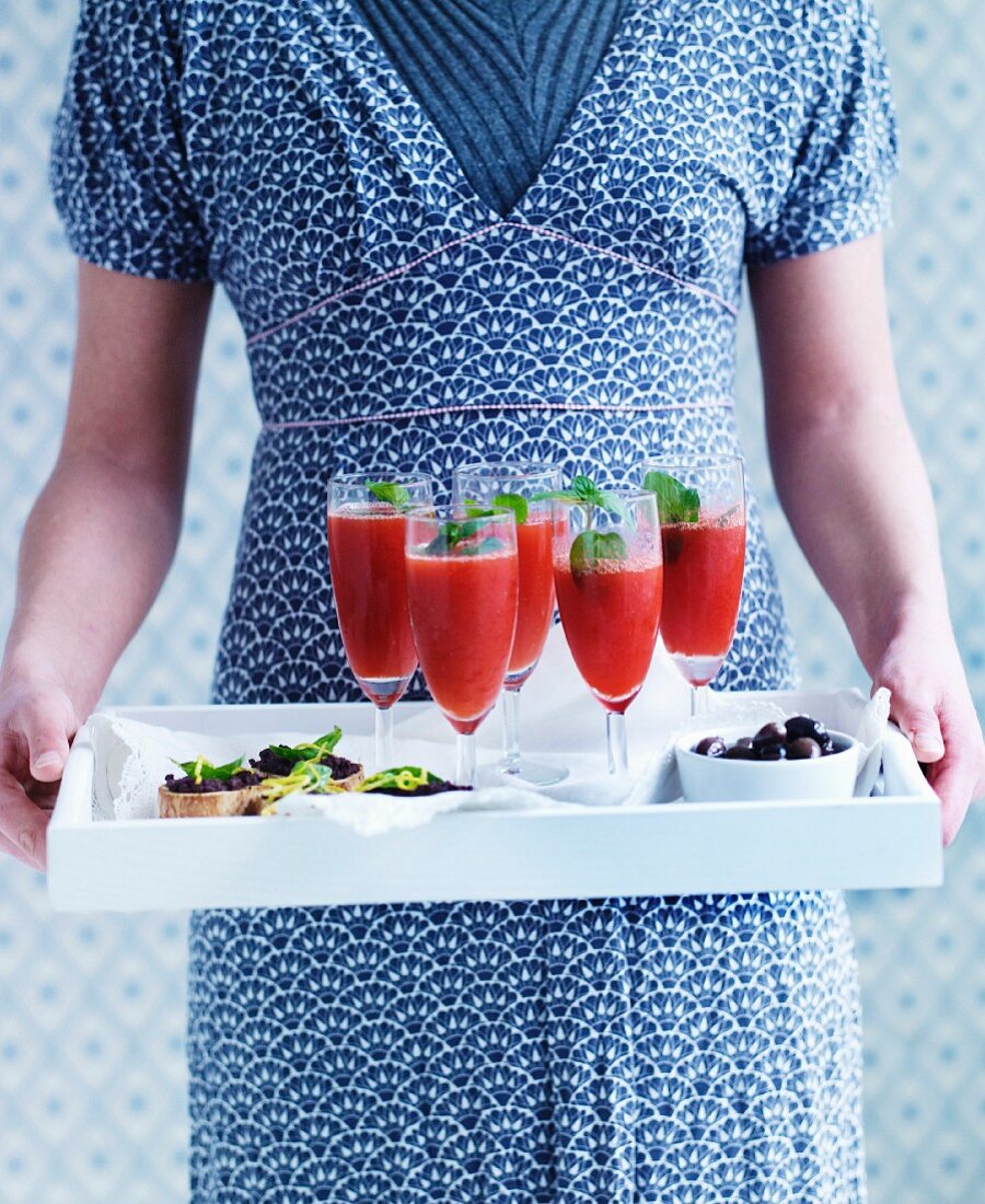 A woman serving champagne cocktails with watermelon and grilled bread with tapenade on a tray