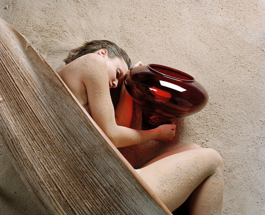 Frau liegt im Sand mit verwittertem Kanu und roter Glasschale