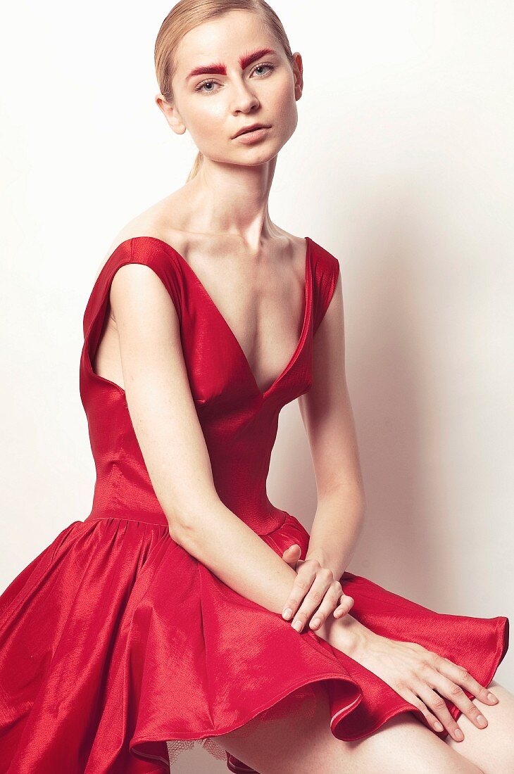 A young woman wearing a red petticoat dress with dyed red eyebrows