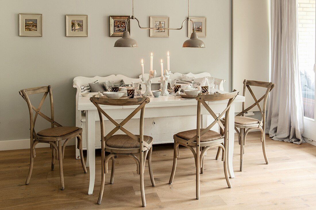 White, set dining table, wooden chairs and lit candles in vintage-style dining room