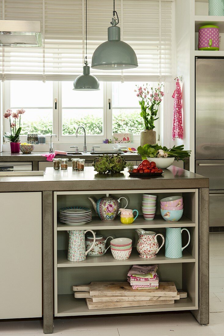 Crockery on base-unit shelves under concrete worksurface below vintage-style pendant lamps