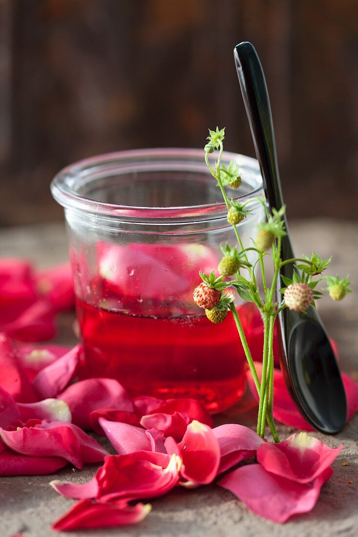 Rose jelly in a jar next to a spoon and rose petals