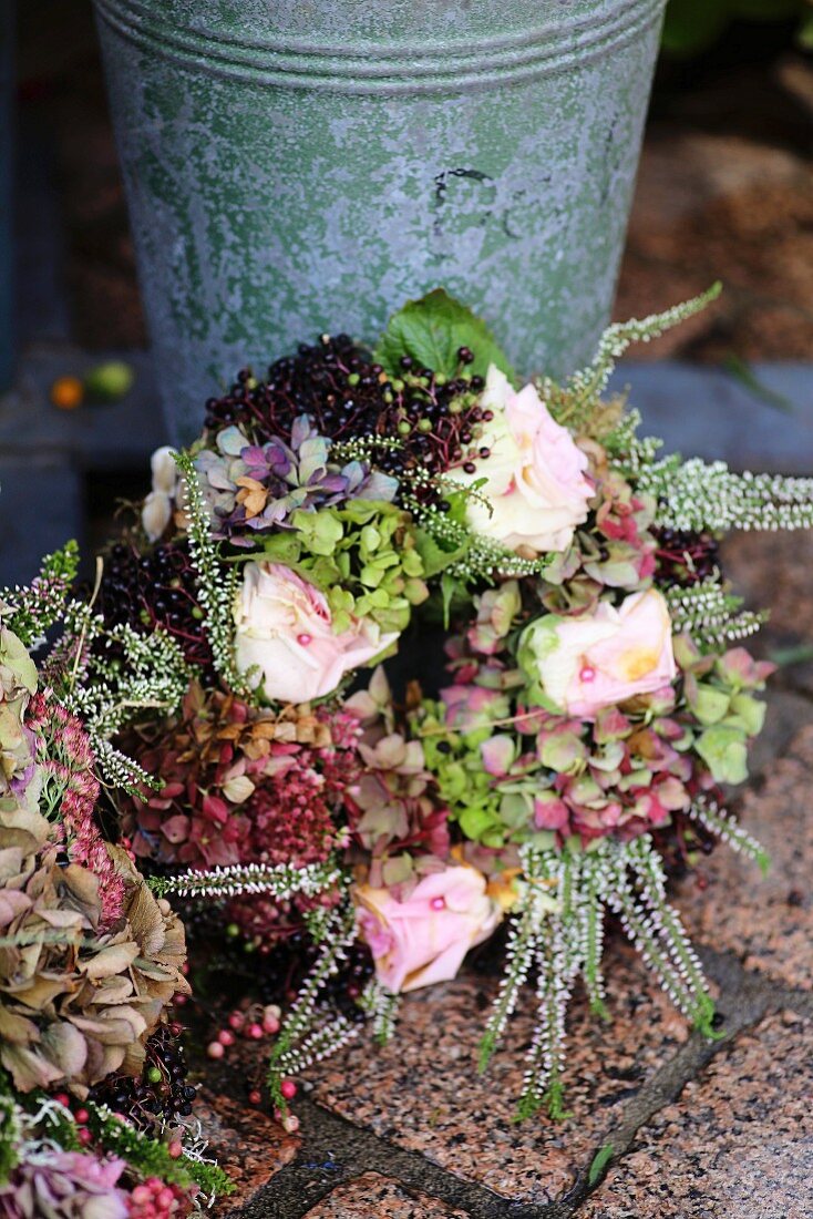 Autumnal wreath of dried hydrangeas, roses, elderberries and heather leaning against zinc bucket