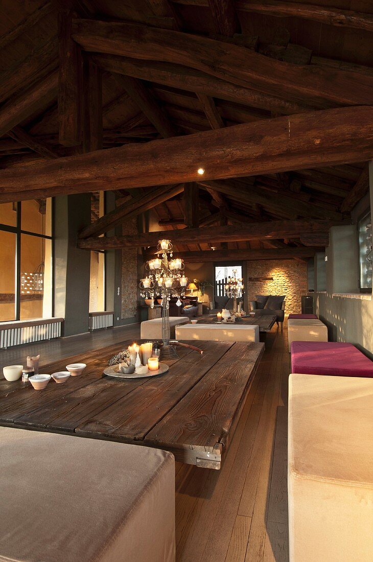 Interior with exposed wooden roof structure, upholstered benches and coffee table with board top