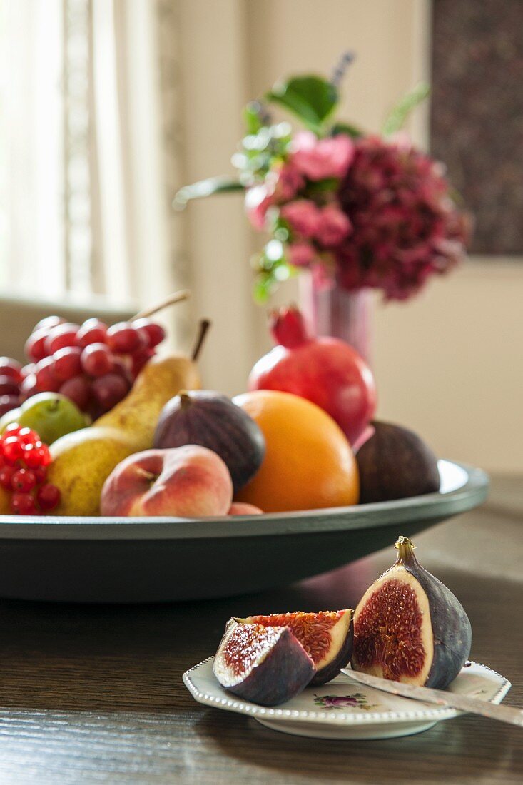 Cut figs on plate and various fruits in large fruit bowl