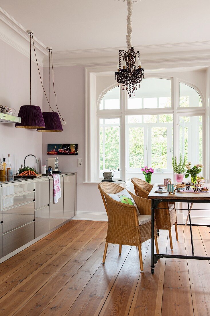 Wicker armchairs and modern, glossy kitchen counter in dining area of period apartment with wooden floor