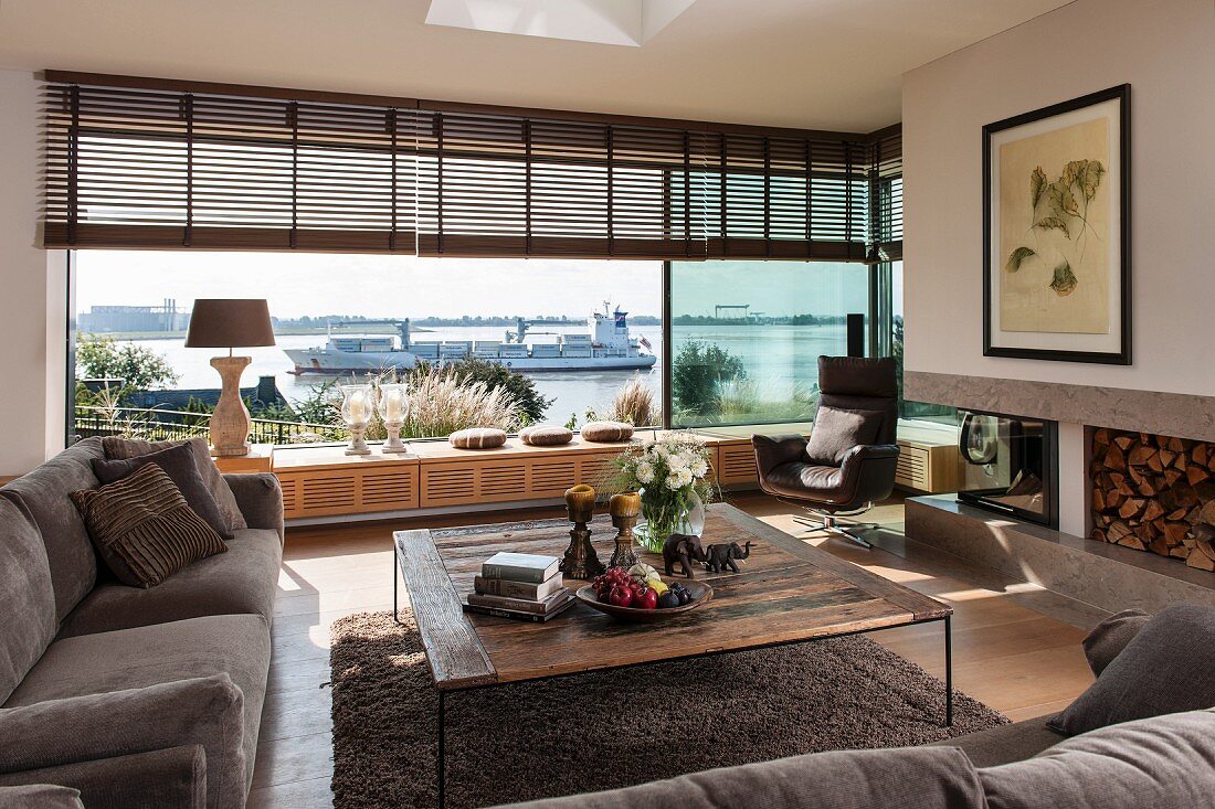 Rustikaler Couchtisch und Polstergarnitur im Wohnzimmer mit Panoramafenster, Blick auf die Elbe und vorbeifahrendes Containerschiff