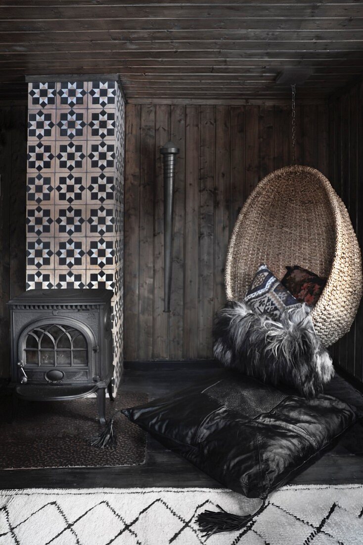 Wicker hanging chair in dark room with wood-burning stove