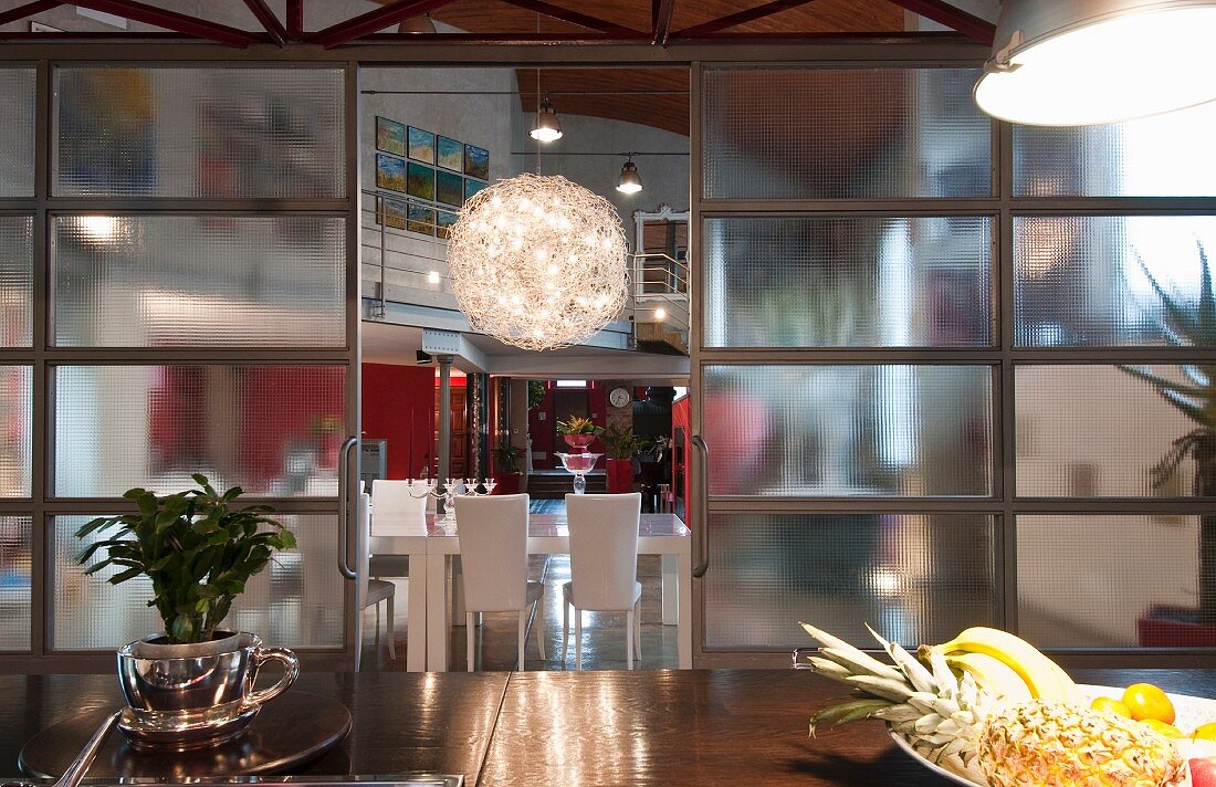 Blick durch Glasschiebetüren im Industrielook auf Essplatz mit Kugel-Lüster in Loftwohnung