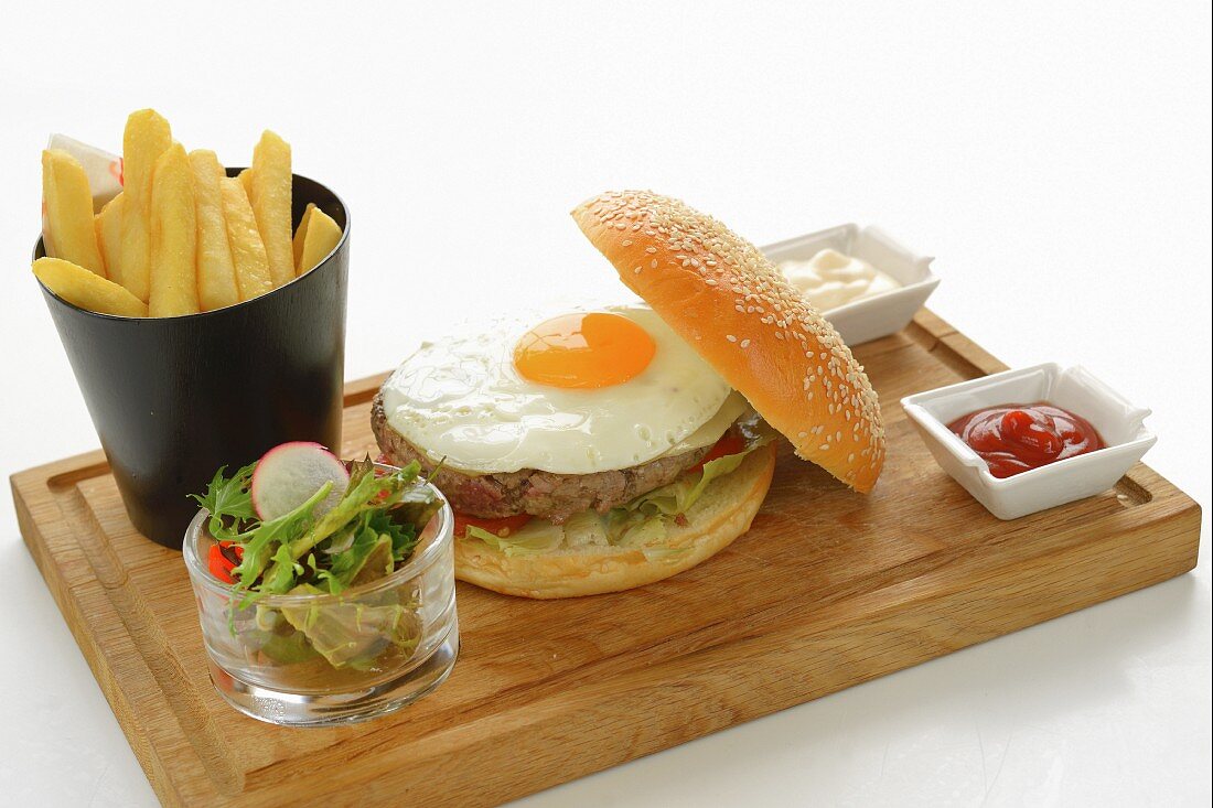 A hamburger with a fried egg served with chips, salad, ketchup and mayonnaise