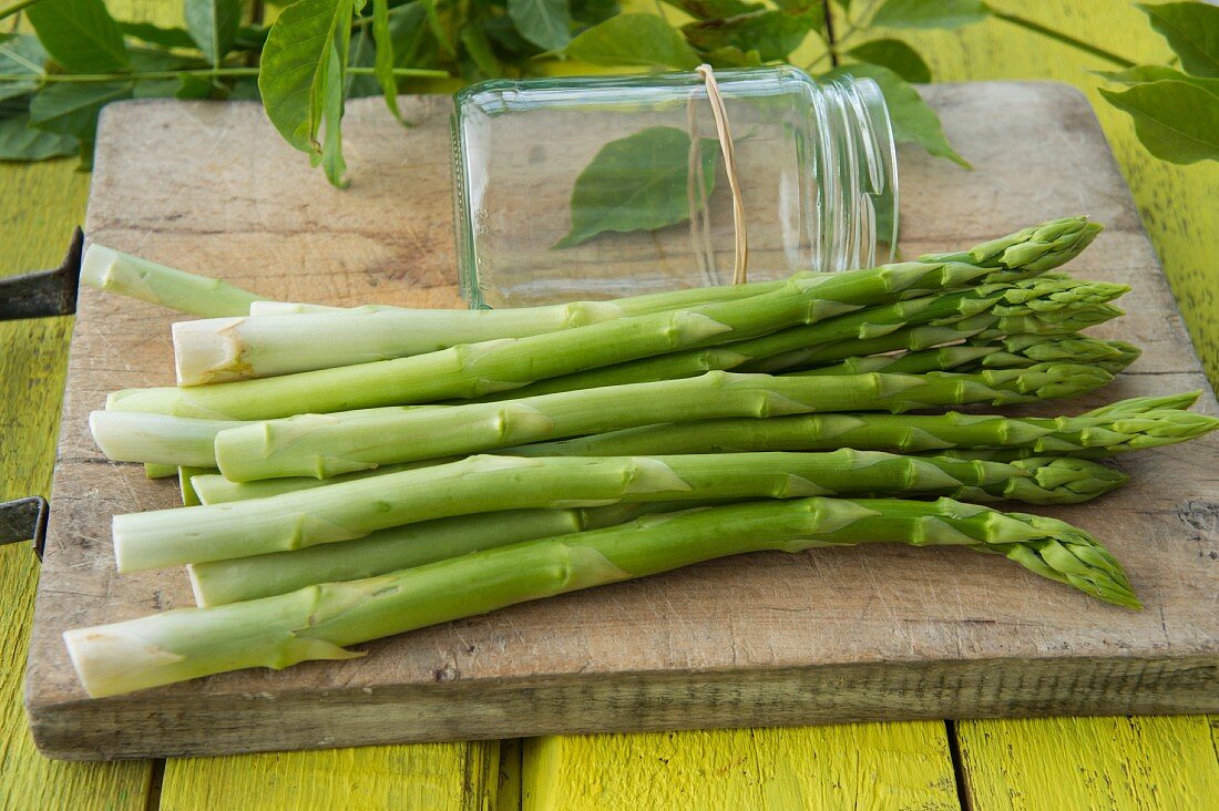 Green asparagus on a wooden board next to a screw-top jar with a rubber band
