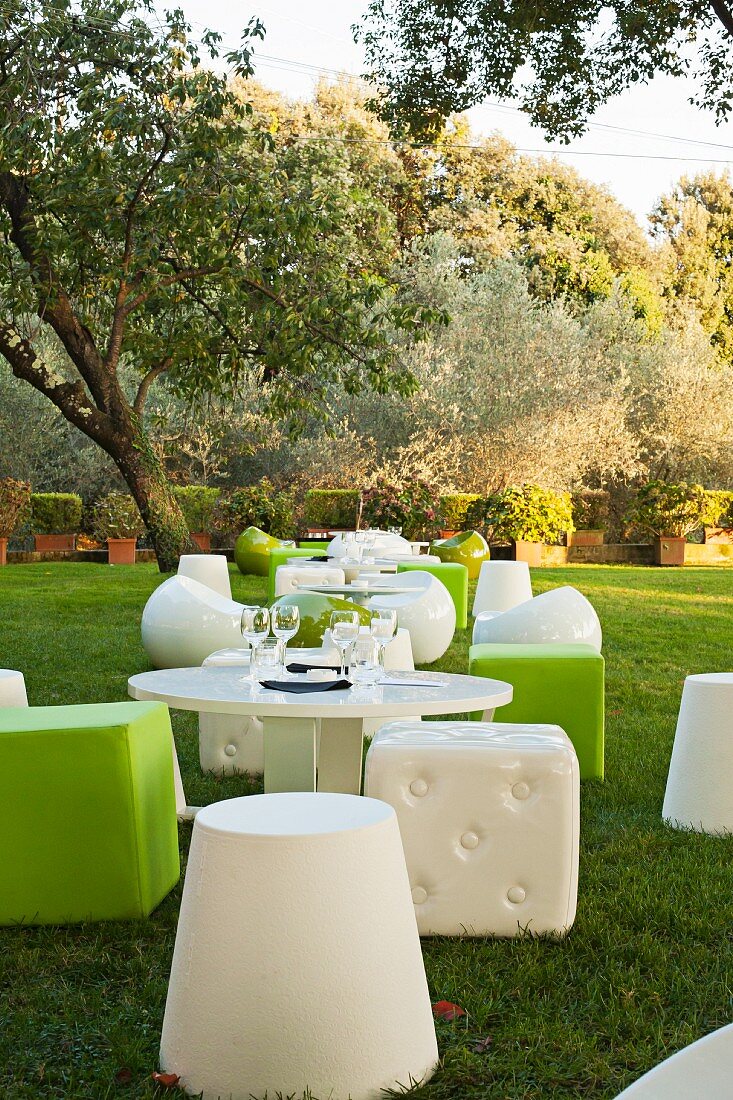Designer outdoor seating in green and white around round tables in the garden