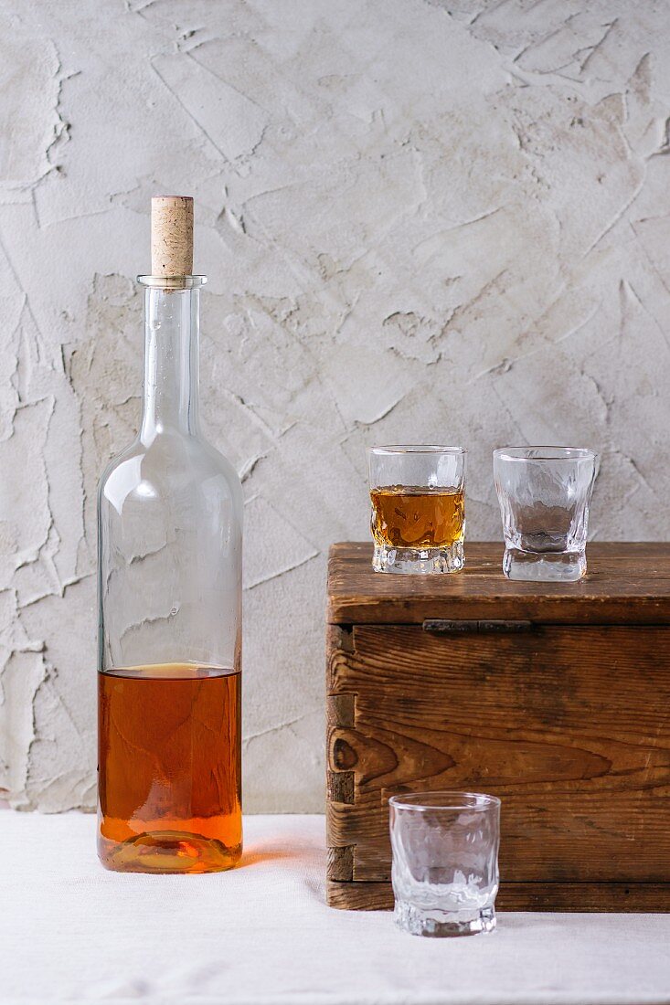 Rumflasche und drei Gläser auf Holztruhe vor verputzter Wand
