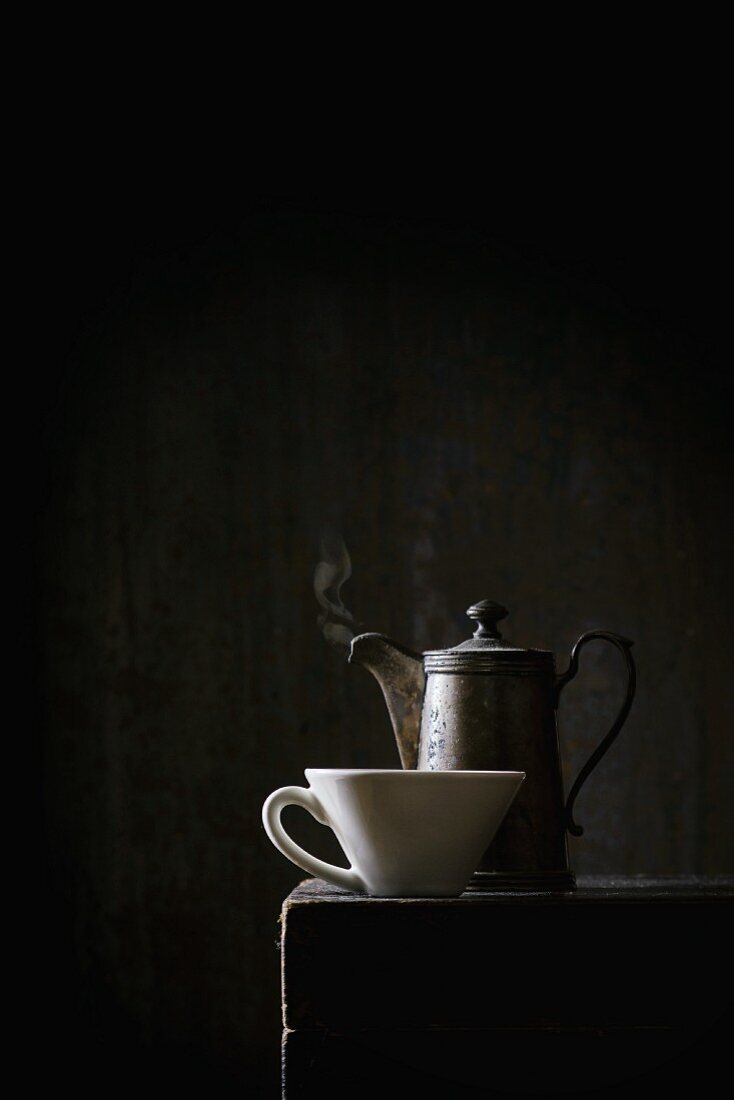 An old coffee pot and a white cup on a black table