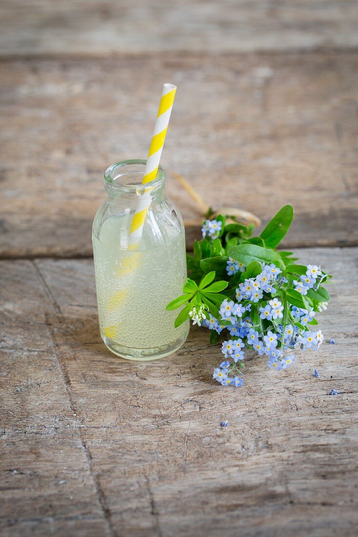 Rhubarb lemonade in a mini glass bottle next to a bouquet of forget-me-nots