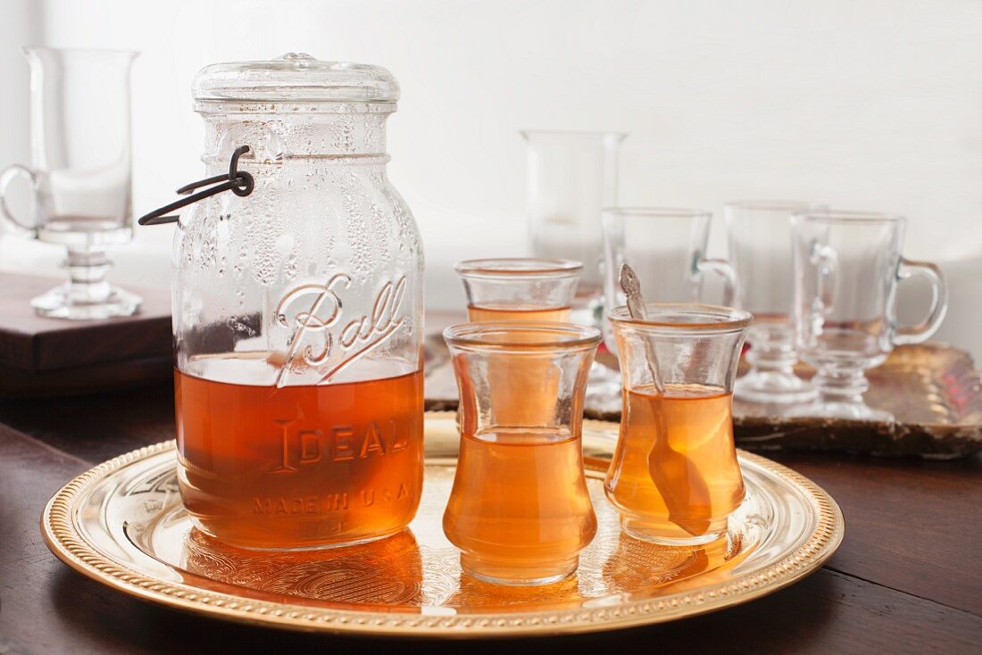 Tea in a glass jug with a handle and tea glasses on a golden tray